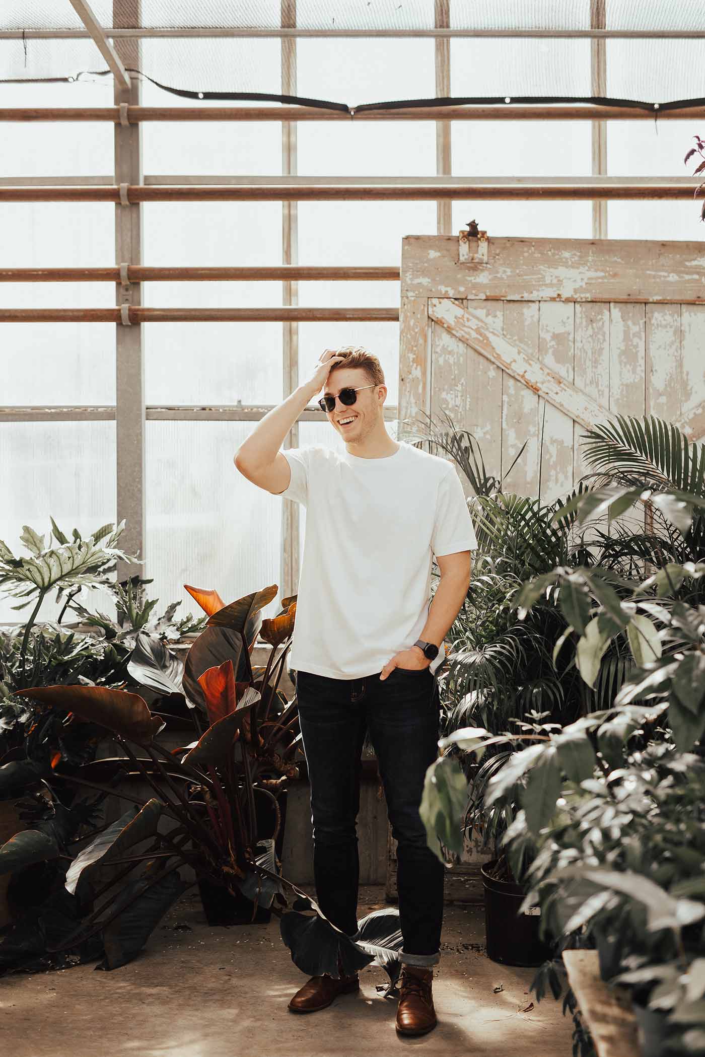 Smiling man wearing a white t-shirt and sunglasses standing in a greenhouse