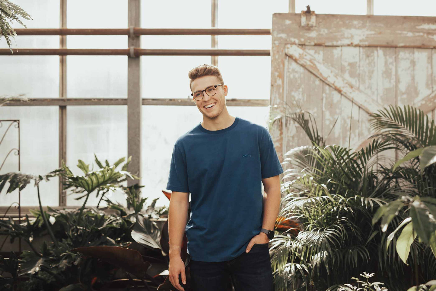 Smiling man wearing a blue t-shirt and standing in a greenhouse